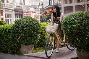 A happy, beautiful young Asian woman is pushing her bicycle on a footpath in the city. photo