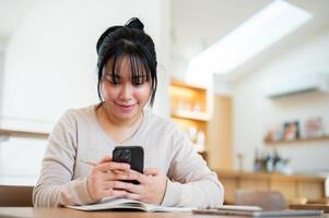 A happy Asian woman is using her smartphone while sitting in a cosy coffee shop. photo