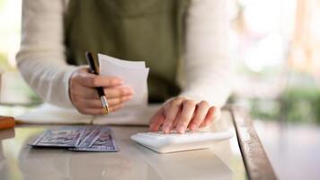 un hembra negocio propietario utilizando un calculadora, revisando ingresos, y gerente su de la tienda finanzas. foto