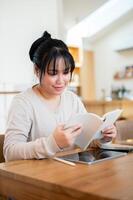 A positive Asian woman is reading book in a cosy coffee shop. photo