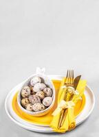 White yellow Easter dishware, quail eggs of natural colors, golden cutlery. Space for menu. Mock up. photo