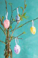 Easter image of spring twigs with young leaves, decorative color eggs hanging on them on turquoise. photo