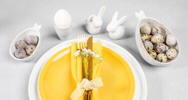 elegante elegante servicio de Pascua de Resurrección mesa en blanco amarillo colores con platos, huevos, cerámico conejitos foto