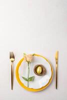Easter gold egg in nest, peach Eustoma flower on plates, gold cutlery on white pink. Copy space. photo