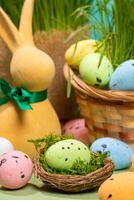 Easter decorative eggs in nest with moss, in basket, on table with yellow bunny and green grass. photo