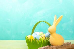 Yellow Easter bunny and green felt basket with decorative colorful eggs on turquoise. Copy space. photo