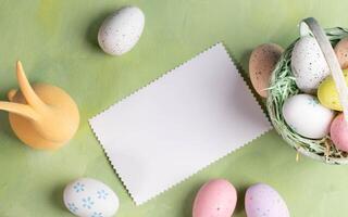 White blank note, decorative Easter eggs, yellow bunny on pastel yellow green backdrop. Top view. photo