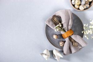 Napkin, vintage cutlery, quail eggs, gray plate, flowers, ceramic bunnies. Gray Easter table setting photo