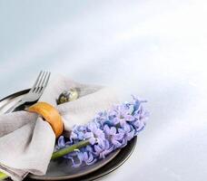 Easter table serving close up. Gray plates, napkin, quail egg, purple jacinth flower on light gray. photo