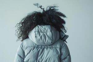 Only a woman with black curly hair in a blue winter jacket on a blue background. Back view photo