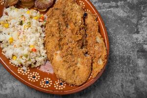 Breaded fried fish and rice in a clay dish on a wooden table. photo