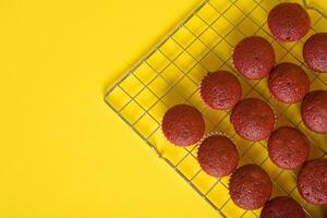 recién horneado rojo terciopelo magdalenas enfriamiento en un amarillo antecedentes. foto