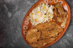 Breaded fried fish and rice in a clay dish on a wooden table. photo