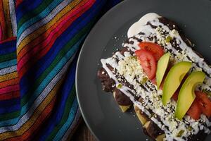 Enfrijoladas served in a clay dish. Typical Mexican food. Bean tacos with cream and cheese. photo