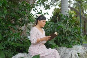 Woman seated next to a tree trunk in a park reading a book. World book day. Concept of reading. photo