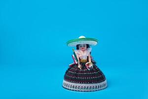 pequeño muñeca representando un mexicano mujer con sombrero y mexicano bandera. aislado figura en azul antecedentes. foto
