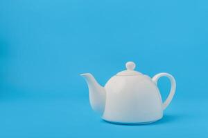 White ceramic teapot isolated on blue background. photo