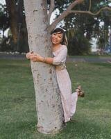 Woman wearing dress and hair bow hugging a tree in a public park. Positive emotion. photo