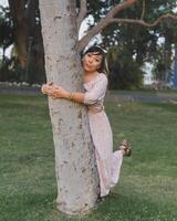 Woman wearing dress and hair bow hugging a tree in a public park. Positive emotion. photo