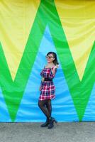 Portrait of woman wearing glasses and plaid dress in front of wall with vibrant colors. photo