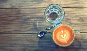 Top view cup of hot art latte coffee and glass of water with beautiful design spoon on wooden table or background with copy space in vintage color style. photo