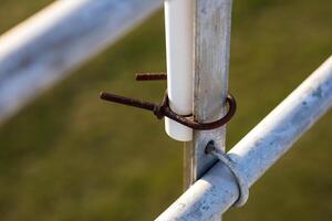 a rusty clamp holding a section of plastic pipe to the back section of some bleachers photo