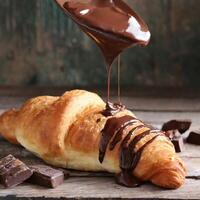 Chocolate falling on croissant fresh baked on wooden table photo