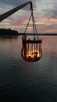 A bonfire burns in a metal basket hanging over the water photo