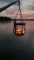 A bonfire burns in a metal basket hanging over the water photo