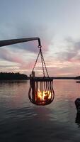 A bonfire burns in a metal basket hanging over the water photo