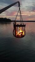 A bonfire burns in a metal basket hanging over the water photo