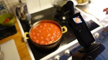 A digital camera is filming homemade meatballs simmering in tomato sauce photo