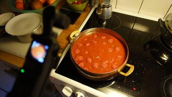 meatballs simmer in tomato sauce as a digital camera shoots photo