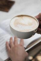 Person Holding Coffee Cup Over Open Book photo