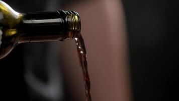 Red wine pours out of the neck of a green wine bottle against an abstract black backdrop. Extreme close-up. Slow motion. 4k video