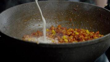 chefe de cozinha derrama creme para dentro uma quente fritar frigideira, que é vapor com a apetitoso e suculento vegetal ensopado fez a partir de milho e grão de bico. fechar acima. lento movimento. 4k video