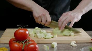 Man grinds a delicious fresh zucchini against a backdrop of other vegetables. He is preparing a vegetarian dish. video