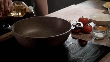 Cook pours sunflower oil into a deep black ceramic frying pan that is standing on an induction hob in the kitchen of the cafe. Close up. Slow motion. 4k video