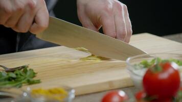 qualifié mains de une professionnel chef habilement trancher citron zeste sur une en bois Coupe conseil, entouré par coloré des légumes sur une foncé Contexte. proche en haut. lent mouvement. 4k video