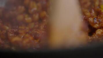 Corn and chickpeas, mixed with red spicy seasoning, are combined with a wooden spoon in a traditional Asian dish. Extreme close-up. Slow motion. 4k video