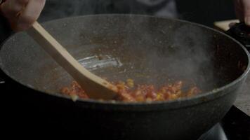 The cook combines chickpeas, corn, and chicken with a variety of spices in a large, black wok using a wooden spoon. Close up. Slow motion. 4k video