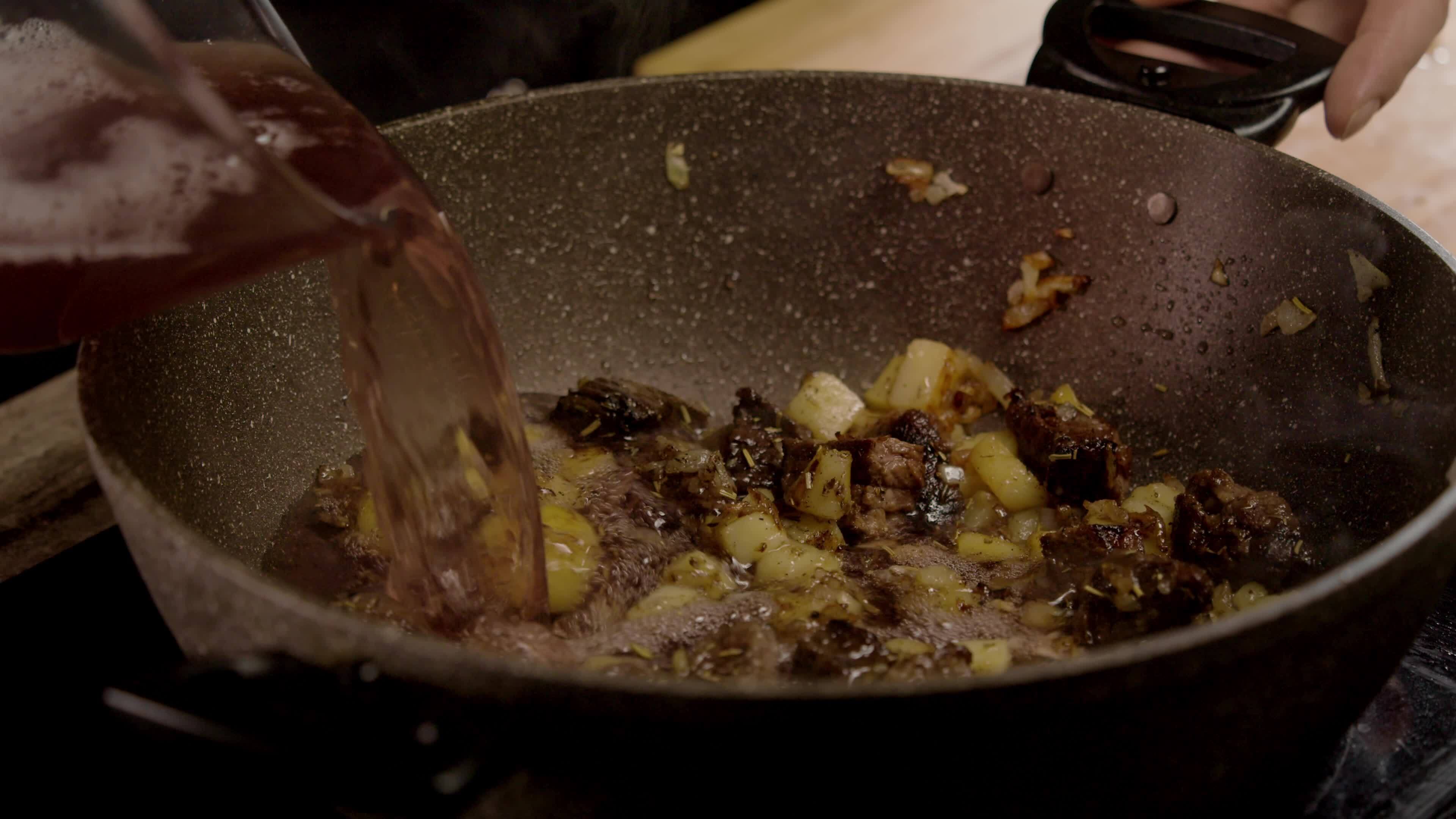 Cook pours the diluted red wine into the deep frying pan, where the
