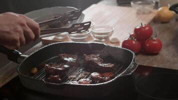 The chef carefully places slices of grilled beef onto a plate using metal tongs in the professional kitchen of a high-end restaurant. Hot oil and fat sizzle and simmer in a pan. Close up. Slow motion. 4k video