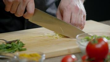 Chef skillfully slices a lemon into thin slices using a large knife on a wooden cutting board in the kitchen of the restaurant, wearing a black uniform. Close up. Slow motion. 4k video