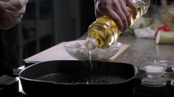een chef in handschoenen giet groente olie in een extreem heet zwart frituren pan. vervolgens ze toevoegen stukken van ongekookt vlees dat hebben geweest uitgebaggerd in meel en koken het. dichtbij omhoog. langzaam beweging. 4k video