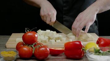 Cook cuts the white squash into large square pieces, while other vegetables are scattered around the kitchen. As the camera moves forward. Close up. Slow motion. 4k video