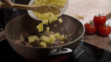 The cook aesthetically adds boiled and sliced potatoes to the meat in a frying pan to create a delicious stew. Close up. Slow motion. 4k video