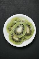 Sliced Kiwi in White Bowl on Black Table photo