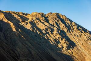 Close up view of a mountain side under direct evening sun light with clear blue sky above. photo