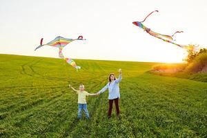 Smiling girl and brother boy standing and holding hands with flying colorful kites on the high grass meadow. Happy childhood moments photo